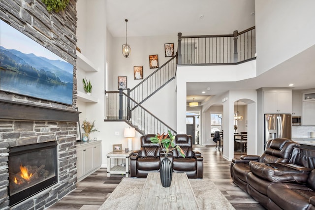 living area with arched walkways, a stone fireplace, wood finished floors, and stairs