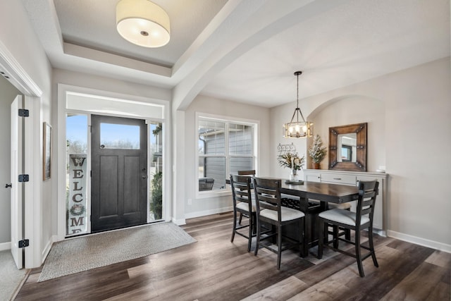 dining space with dark wood finished floors, a raised ceiling, a notable chandelier, and baseboards