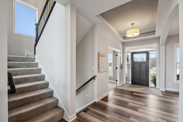 foyer entrance with a tray ceiling, baseboards, wood finished floors, and stairway