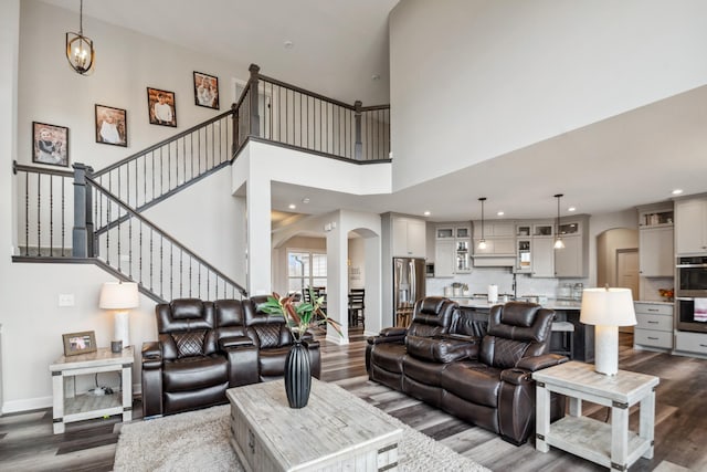 living area featuring stairway, dark wood-style floors, baseboards, arched walkways, and a towering ceiling