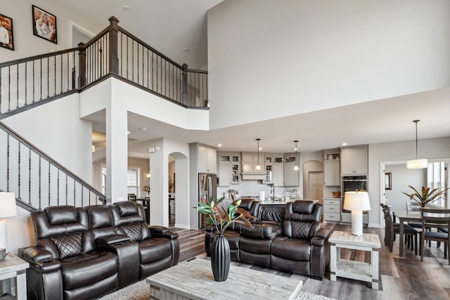 living room featuring stairs, a high ceiling, wood finished floors, and arched walkways