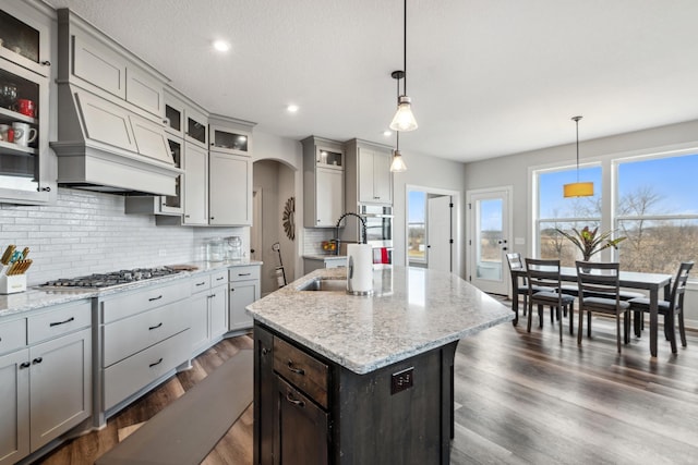 kitchen with a kitchen island with sink, a sink, backsplash, dark wood-style floors, and arched walkways