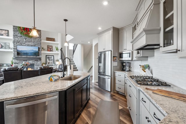 kitchen featuring dark wood-style floors, custom exhaust hood, a sink, a stone fireplace, and appliances with stainless steel finishes