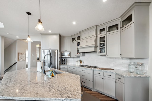 kitchen with backsplash, light stone counters, arched walkways, stainless steel appliances, and a sink