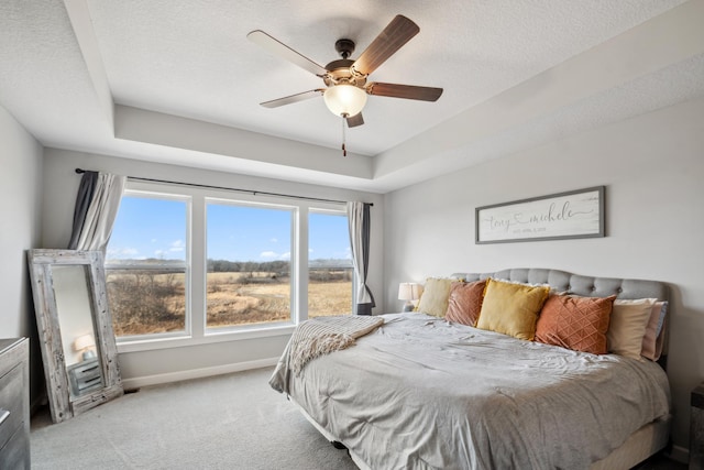 bedroom featuring baseboards, carpet, a textured ceiling, a raised ceiling, and a ceiling fan