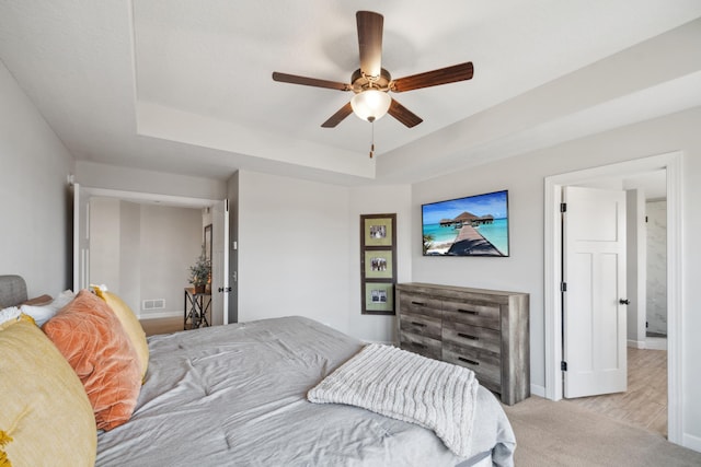 bedroom featuring visible vents, a ceiling fan, a tray ceiling, carpet flooring, and baseboards