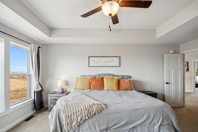 bedroom with visible vents, a ceiling fan, a tray ceiling, baseboards, and light colored carpet