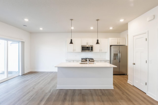 kitchen with appliances with stainless steel finishes, white cabinetry, hanging light fixtures, light hardwood / wood-style floors, and a center island with sink