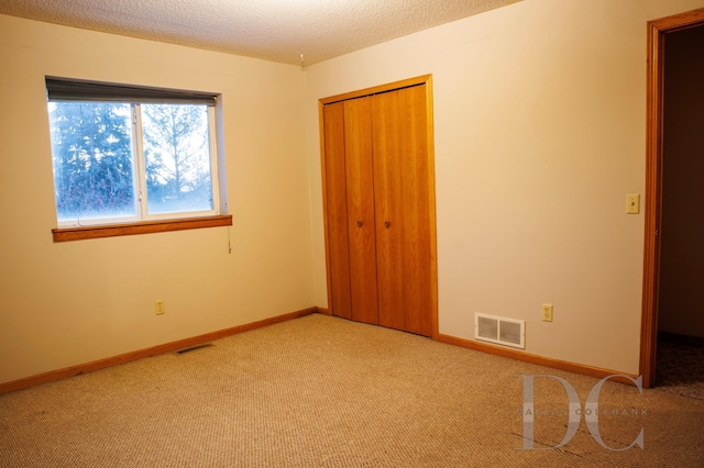 unfurnished bedroom featuring a textured ceiling, a closet, visible vents, and light colored carpet