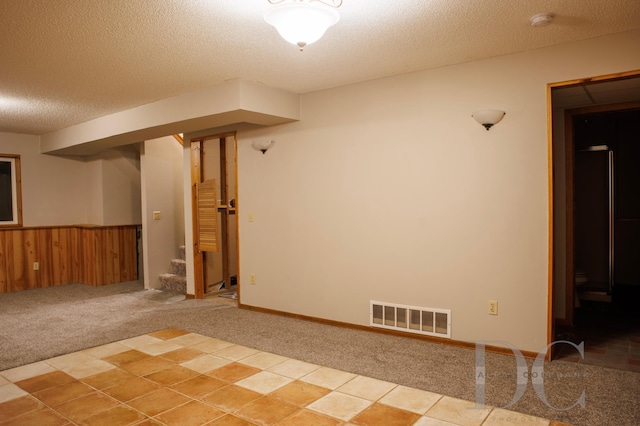 unfurnished room featuring visible vents, wainscoting, light colored carpet, stairs, and a textured ceiling