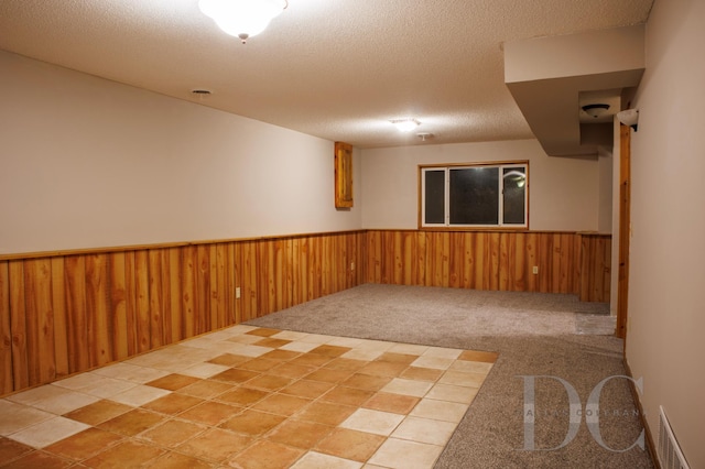 spare room with a textured ceiling, wooden walls, carpet floors, visible vents, and wainscoting