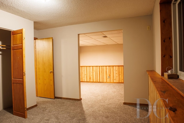 corridor with a drop ceiling, wainscoting, carpet, a textured ceiling, and wood walls