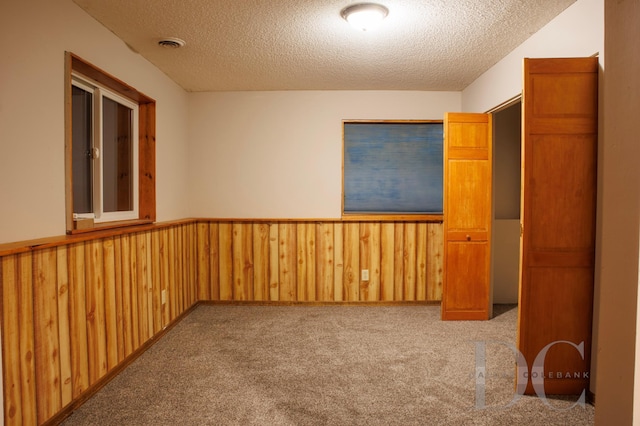 carpeted spare room with a wainscoted wall, a textured ceiling, visible vents, and wooden walls