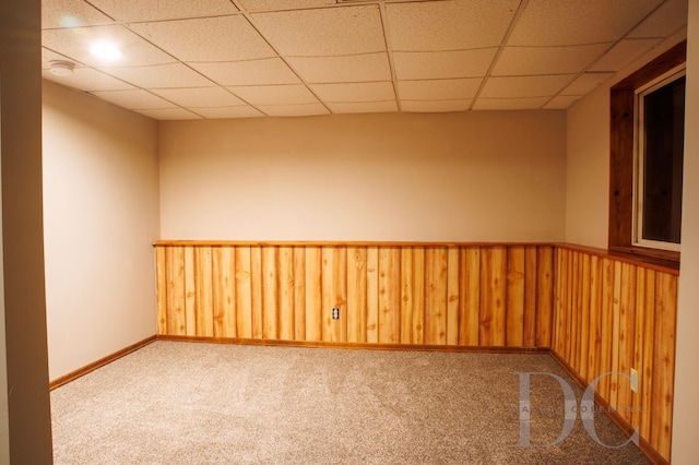 unfurnished room with carpet, a drop ceiling, wainscoting, and wooden walls