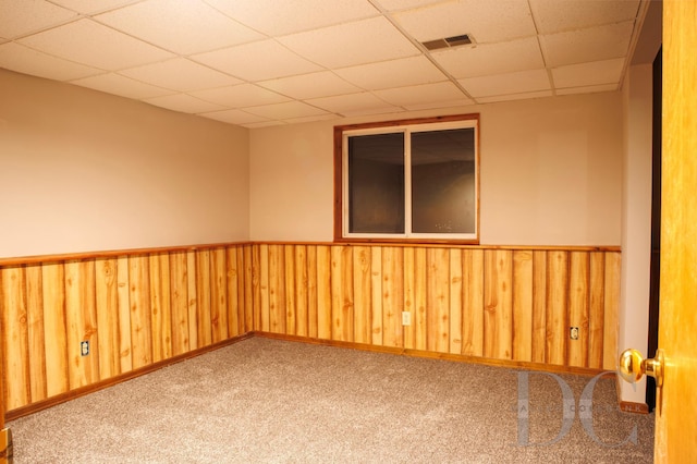 carpeted empty room with a wainscoted wall, a drop ceiling, visible vents, and wooden walls