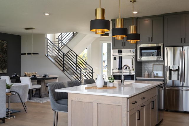 kitchen with decorative light fixtures, stainless steel appliances, hardwood / wood-style flooring, and an island with sink