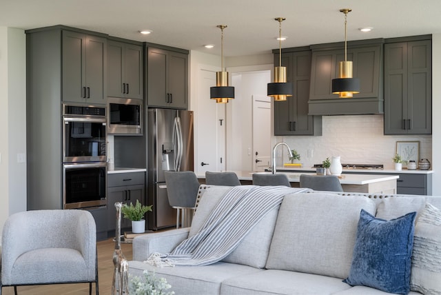 kitchen featuring hanging light fixtures, stainless steel appliances, backsplash, a center island with sink, and light wood-type flooring