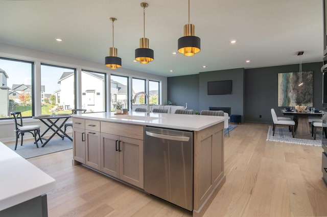 kitchen with stainless steel dishwasher, sink, decorative light fixtures, a center island with sink, and light hardwood / wood-style floors