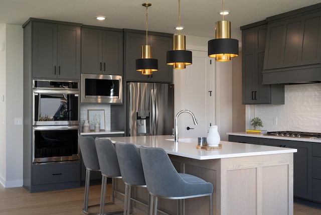 kitchen featuring stainless steel appliances, a kitchen breakfast bar, pendant lighting, a center island with sink, and light wood-type flooring