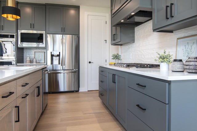 kitchen with gray cabinetry, light hardwood / wood-style flooring, range hood, and appliances with stainless steel finishes