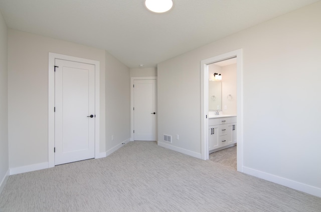 unfurnished bedroom featuring a closet, light colored carpet, and ensuite bath