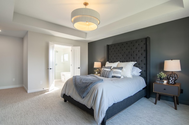 bedroom with carpet flooring, connected bathroom, and a tray ceiling