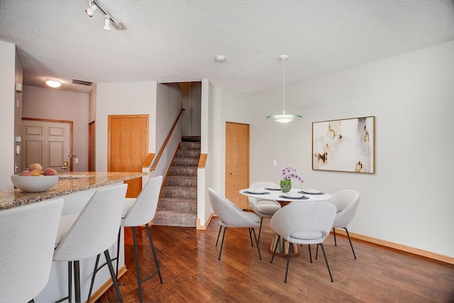 dining area with rail lighting, dark hardwood / wood-style flooring, and a textured ceiling