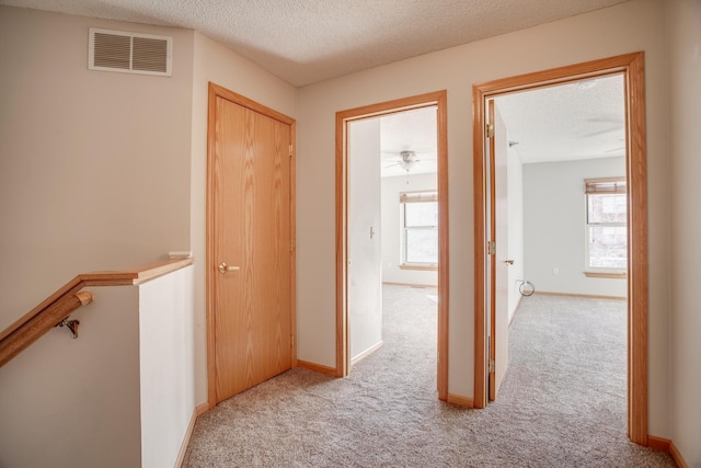 hall with light colored carpet and a textured ceiling