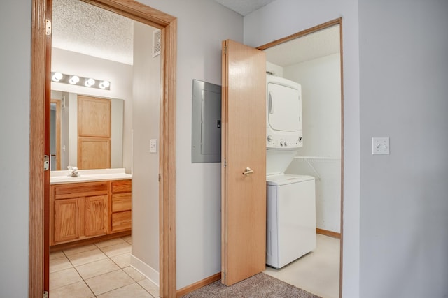 laundry room with a textured ceiling, electric panel, stacked washing maching and dryer, and sink