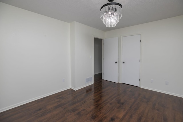 spare room featuring dark hardwood / wood-style flooring, a textured ceiling, and a notable chandelier