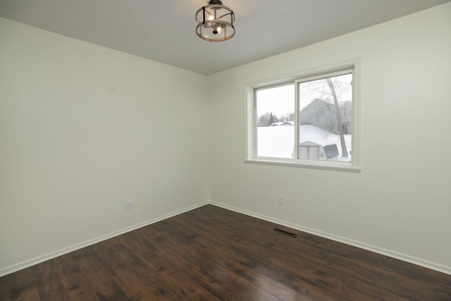 empty room with dark hardwood / wood-style flooring and an inviting chandelier