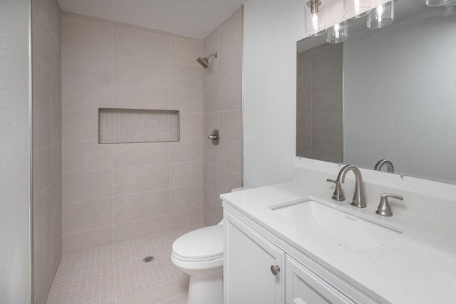 bathroom featuring a tile shower, vanity, and toilet