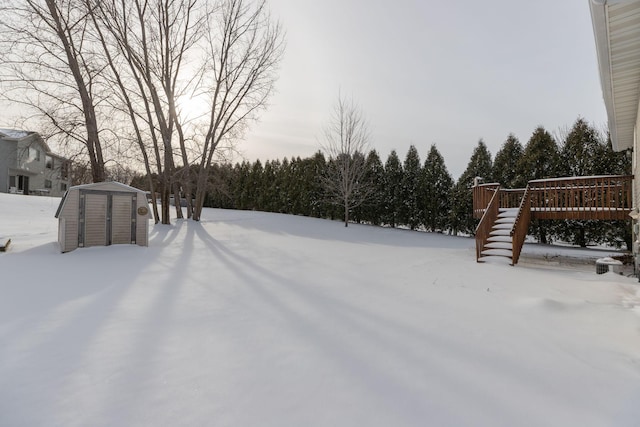 snowy yard with a wooden deck and a storage unit