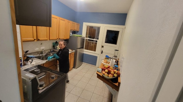 kitchen with electric range, sink, backsplash, stainless steel fridge, and light tile patterned floors