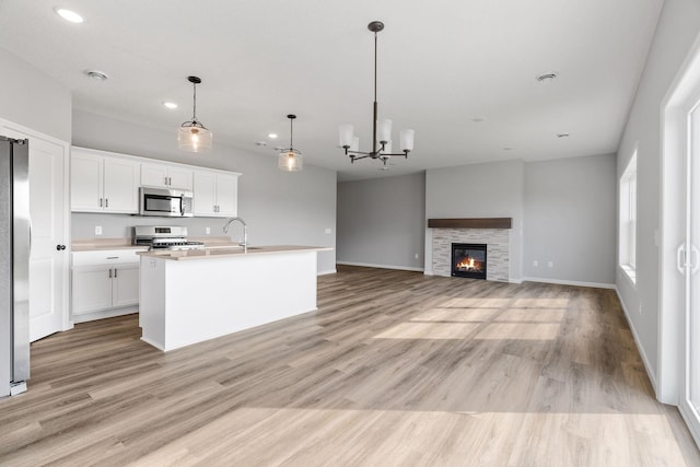 kitchen with white cabinetry, appliances with stainless steel finishes, a kitchen island with sink, and decorative light fixtures