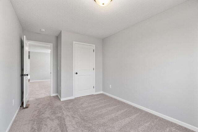 unfurnished bedroom with light colored carpet, a closet, and a textured ceiling