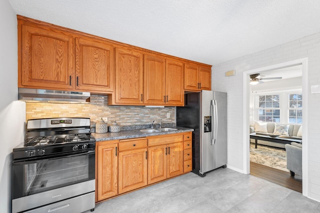 kitchen with sink, stainless steel appliances, dark stone counters, a textured ceiling, and decorative backsplash