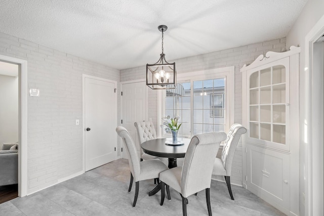 dining space with brick wall, a textured ceiling, and an inviting chandelier