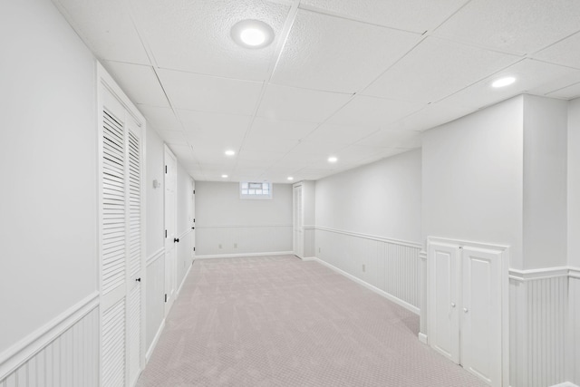 basement featuring a paneled ceiling and light colored carpet