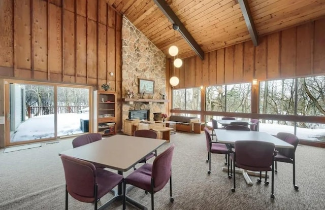 carpeted dining room featuring wooden ceiling, high vaulted ceiling, wooden walls, a fireplace, and beamed ceiling