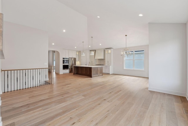 kitchen with pendant lighting, light hardwood / wood-style floors, stainless steel refrigerator, and an island with sink