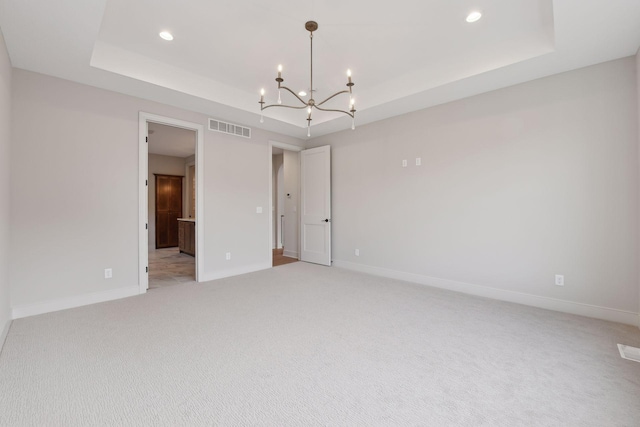 unfurnished room featuring a tray ceiling, an inviting chandelier, and light colored carpet