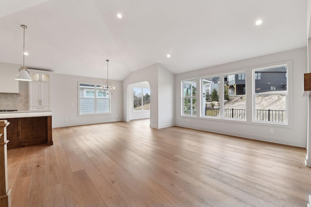 unfurnished living room with light hardwood / wood-style flooring, a chandelier, and vaulted ceiling