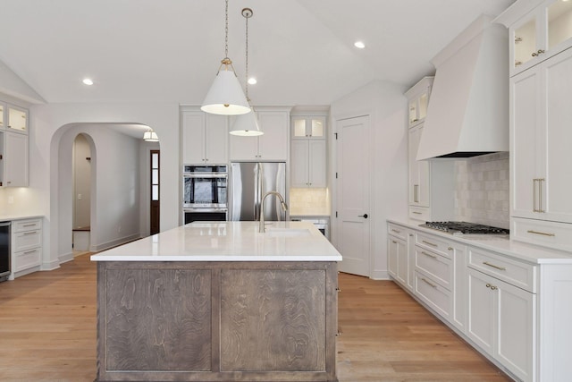 kitchen featuring sink, stainless steel appliances, lofted ceiling, a center island with sink, and custom exhaust hood