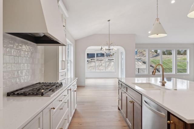 kitchen with sink, pendant lighting, white cabinets, custom range hood, and appliances with stainless steel finishes