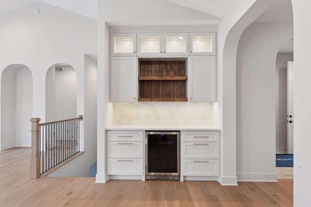 bar featuring tasteful backsplash, white cabinetry, light hardwood / wood-style flooring, high vaulted ceiling, and wine cooler