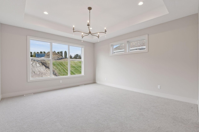 carpeted empty room featuring a tray ceiling and an inviting chandelier