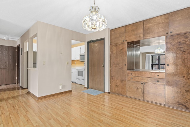 kitchen with light wood-type flooring, white range oven, an inviting chandelier, white cabinetry, and hanging light fixtures