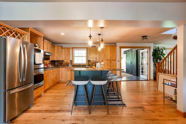 kitchen with pendant lighting, a kitchen island, light wood-type flooring, and appliances with stainless steel finishes