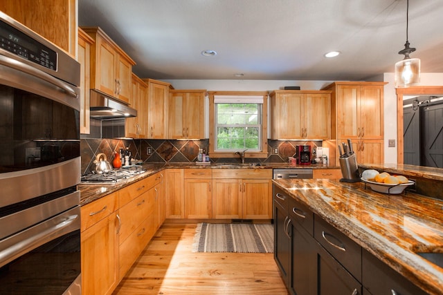 kitchen featuring sink, stainless steel appliances, hanging light fixtures, dark stone counters, and light wood-type flooring